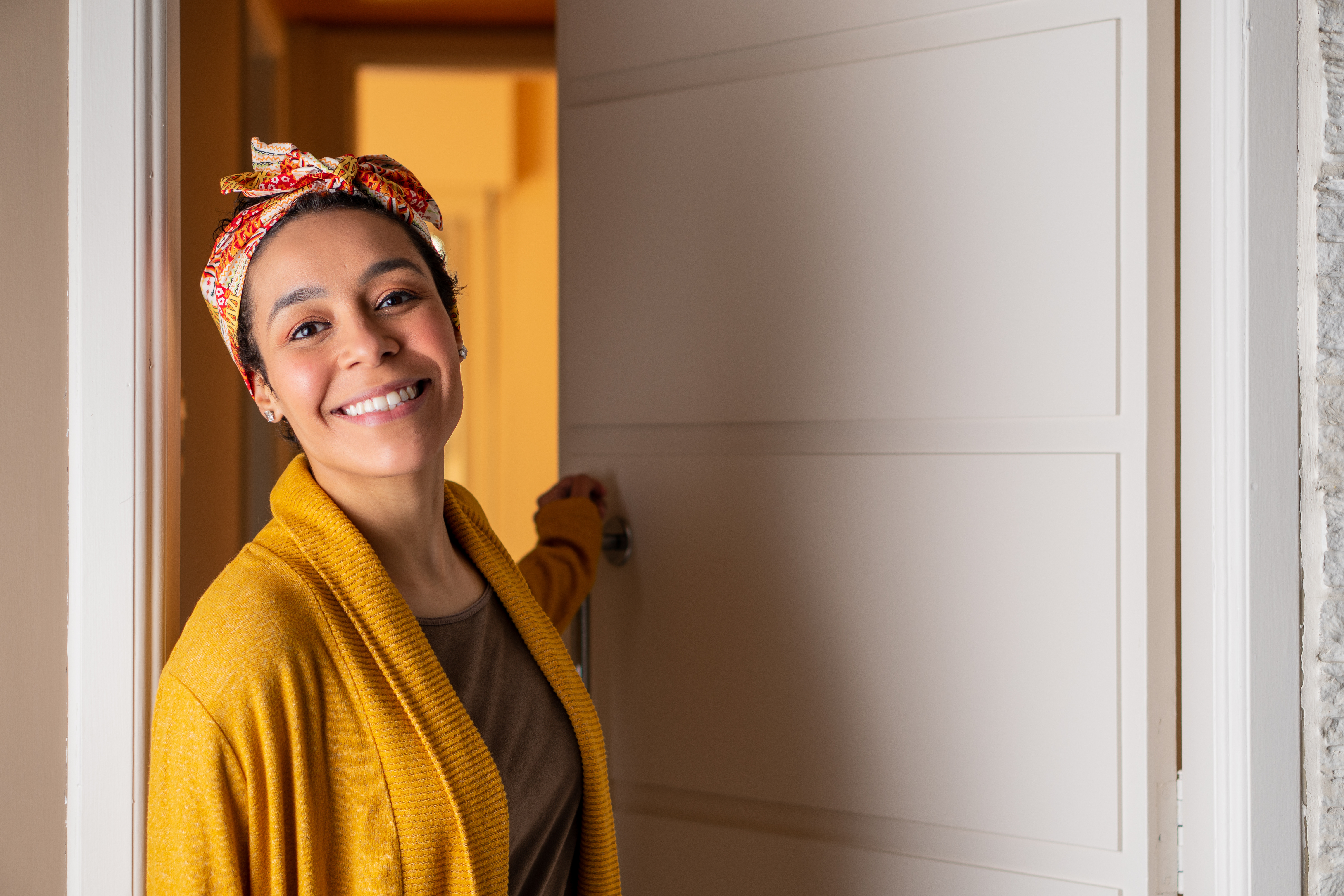 Close up of smilingblack woman with head band leaving home during the day. In front of apartment door. Individuality, style, identity concept.