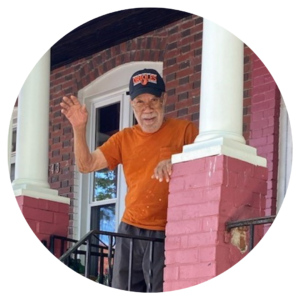 Man waves from his front porch with an Orioles cap and orange shirt. 